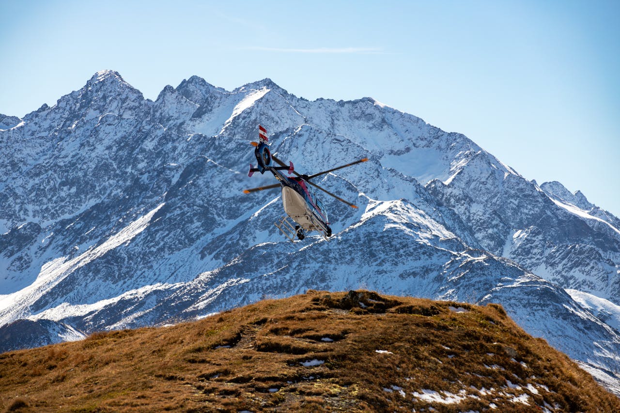 A helicopter flies over the snowy peaks of the Korutany mountains on a clear day.